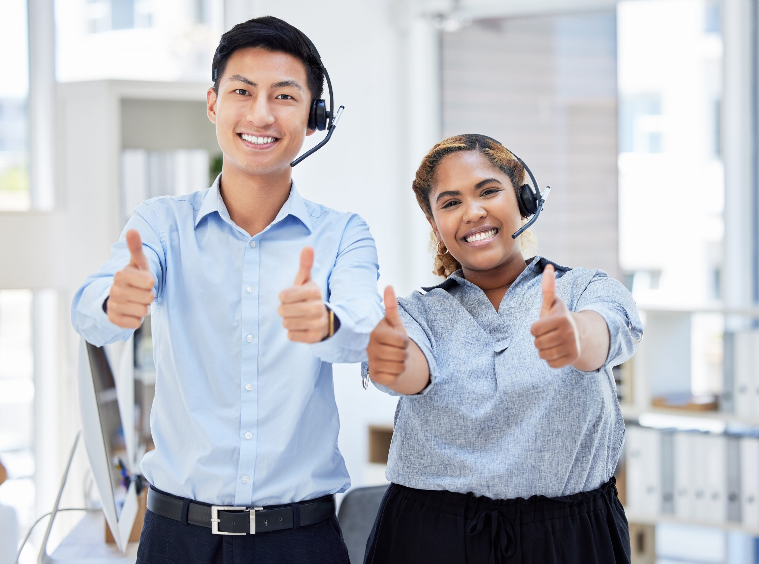 Two young happy male and female call center agents showing thumbs up while answering calls working .